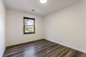 A second bedroom with plank floors, bright white walls and a window