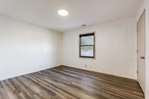 A fourth bedroom with plank floors and white walls with a window